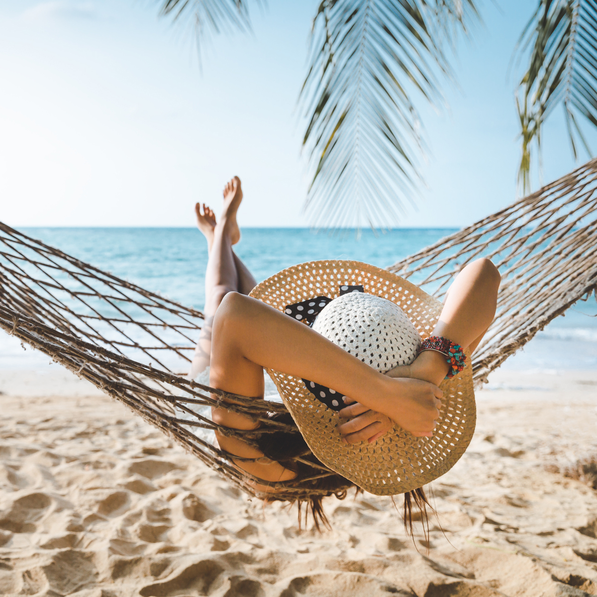 Person sits in hammock with sun hat on the beach