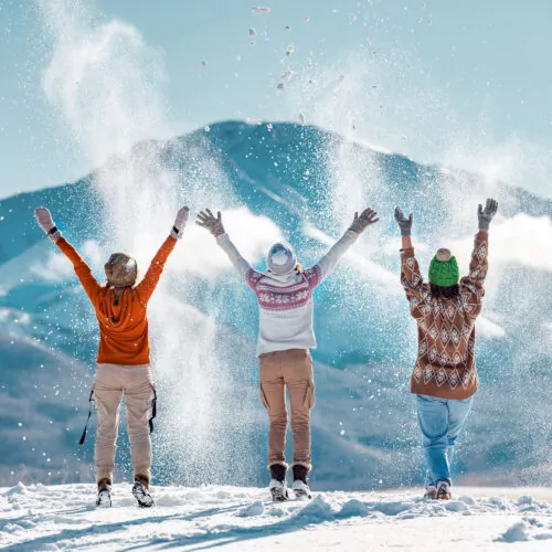 3 people throw snow with moutain in background